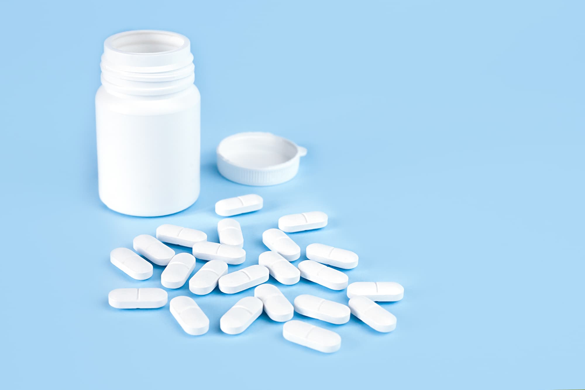 A pill bottle and white pills on a blue surface.
